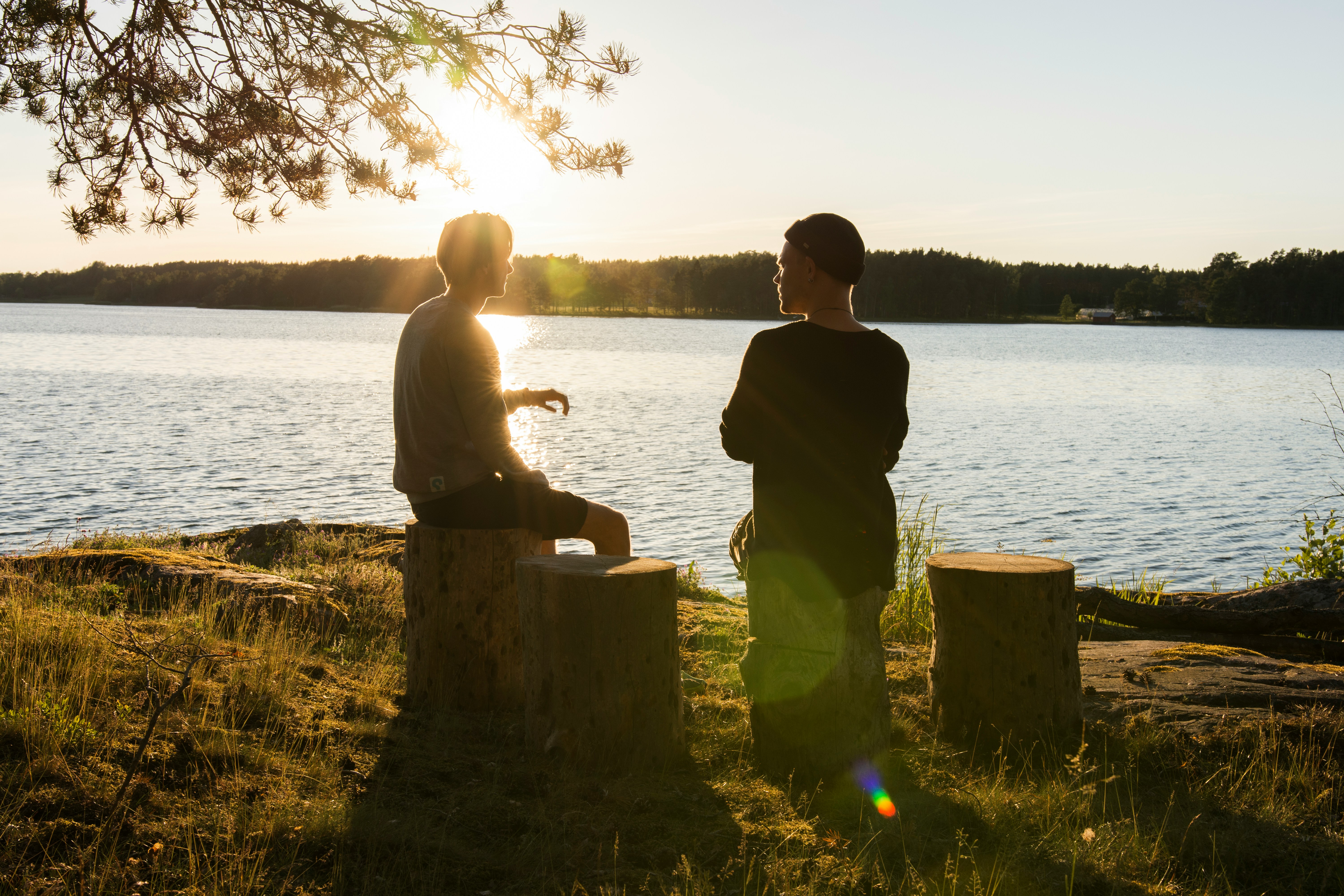 two young men sitting by a lake on tree stumps